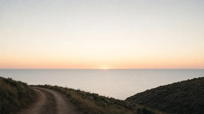 Horizonte marino al amanecer, con un camino de tierra que se acerca a la línea del agua.