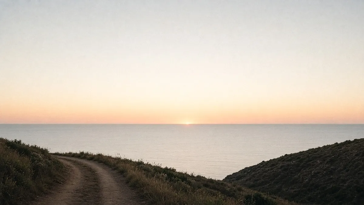 Horizonte marino al amanecer, con un camino de tierra que se acerca a la línea del agua.
