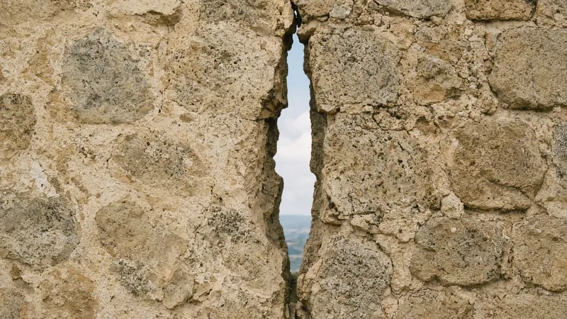 Muro de piedra con una grieta vertical por la que entra la luz del día.